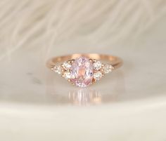 an oval shaped pink diamond ring with three smaller diamonds around it on a white surface