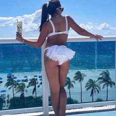 a woman in a white bathing suit standing on a balcony looking out at the ocean