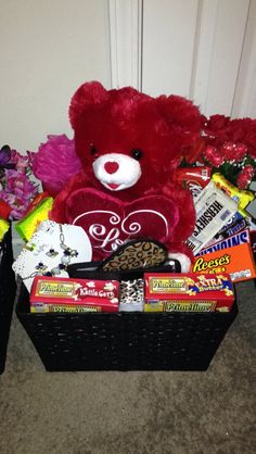 a red teddy bear sitting next to a basket filled with candy and candies on the floor