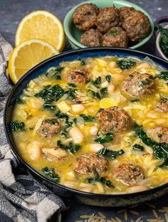 a bowl of soup with meatballs, spinach and lemons on the side