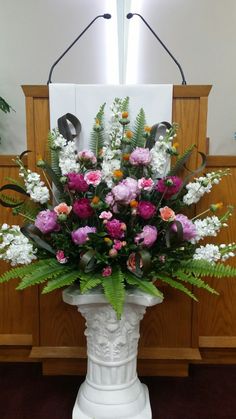 a white vase filled with lots of colorful flowers on top of a table next to a podium