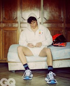 a man sitting on top of a bed with his legs crossed and wearing tennis shoes