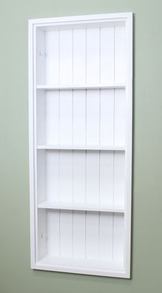 an empty white book shelf against a green wall