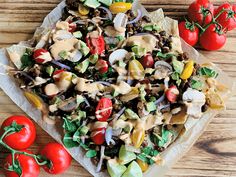 a salad with dressing and tomatoes on a wooden table next to some tortilla chips