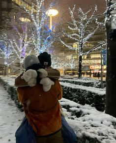 a person walking down a snowy street with snow on the ground and lights in the background