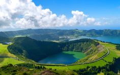 an aerial view of a lake surrounded by green hills and trees with clouds in the sky