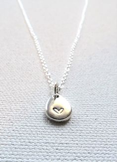 A tiny, delicate silver-plated teardrop hand stamped with a heart hangs from a delicate chain.  The lightweight teardrop is stamped by hand with a tiny heart.  Each silver plated textured teardrop charm (base metal of zinc alloy - lead and nickel free) measures 11 mm x 8 mm.  Due to the handmade nature of the necklace, no two are identical.  The irregular and slight imperfections are what set hand stamped jewelry apart from factory made pieces and offer a whimsical charm.  This is a wonderful gift for an anniversary, Valentine's Day, wedding, cancer support, everyday wear, or to celebrate the life or loss of an infant or loved one. Each piece is hand crafted when ordered so please allow 3-5 days for design creation.  Select chain length from drop down box.  An optional recycled glass bead Handmade Sterling Silver Charm Necklaces With Teardrop Pendant, Handmade Sterling Silver Charm Necklace With Teardrop Pendant, Handmade Sterling Silver Teardrop Charm Necklace, Nickel Free Teardrop Sterling Silver Charm Necklace, Nickel-free Teardrop Sterling Silver Charm Necklace, Nickel-free Teardrop Charm Necklace In Sterling Silver, Handmade Teardrop Sterling Silver Charm Necklaces, Handmade Teardrop Sterling Silver Charm Necklace, Dainty Teardrop Heart Charm Jewelry