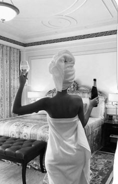 a woman with a towel on her head is holding a wine glass in front of the bed