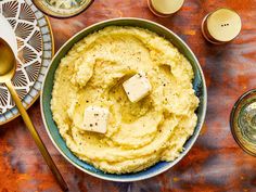 mashed potatoes in a bowl with butter and seasoning next to it on a table