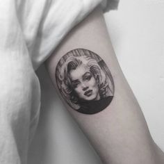 a black and white photo of a woman's face in a circle tattoo on the arm