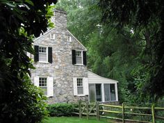 a stone house with shutters on the front and side windows is surrounded by greenery