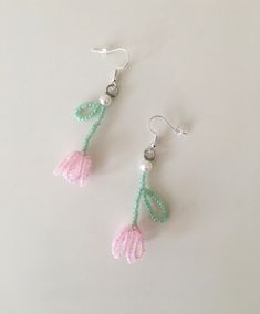 two pink and green flowers are hanging from the earwires on white table top