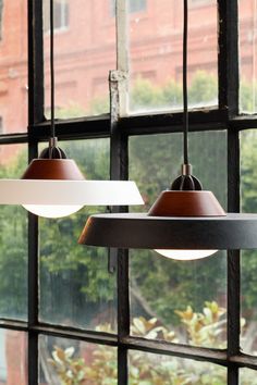 two hanging lights in front of a window with trees outside the windowsills, one light brown and one white