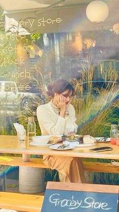 a woman sitting at a table in front of a store window with her hand on her face