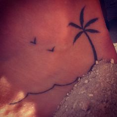 a small palm tree tattoo on the side of someone's foot, with birds flying over it