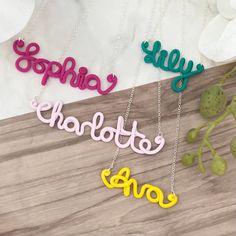 three name necklaces with the word charlotte in different colors on a wooden table next to flowers