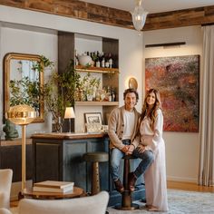 a man and woman sitting on a stool in a living room