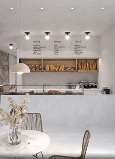 a white table and chairs in front of a bakery counter with breads on it