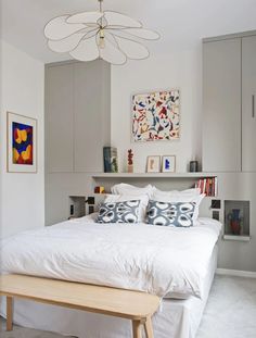 a white bed sitting under a chandelier next to a wooden bench in a bedroom