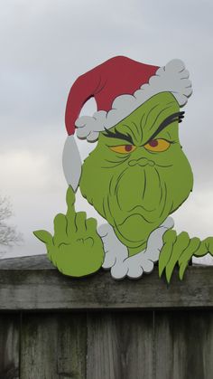 the grin face is wearing a santa hat and pointing his finger at something on top of a wooden fence