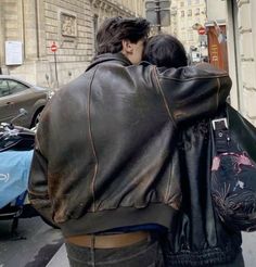 two people are walking down the street with their backs to each other and one person is wearing a leather jacket