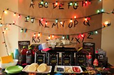 a table topped with lots of different foods and desserts next to a wall covered in lights