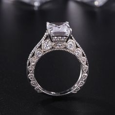 Make the moment you ask her to marry memorable with this sparkling vintage-inspired ring. It features a shimmering emerald cut center stone while additional stones are set into the shank to assure sparkle from every angle. Milgrain detailing along the ring's shank adds depth and dimension to this elegant design. This engagement ring is a beautiful beginning to your romantic love story.Carat Weight: 5.2 ctStone Size: 8*10 mmStone Type: Jeulia® StoneNumber of Stones: 1 Stone Color: Diamond WhiteStone Shape: RadiantCarat Weight: 1.445 ctStone Size: 1.75,1.5,2.3 mmStone Type: Jeulia® StoneNumber of Stones: 26 Stone Color: Diamond WhiteStone Shape: RoundWeight: 5.35 gWidth: 10.2 mmHeight: 8.62 mmThickness: 3.4 mmMaterial: 925 SilverPlating Color: Silver Square Cut Moissanite Rings With Diamond Accents For Weddings, Luxury Square Cut Ring For Promise, Luxury Square Cut Rings For Promises, Wedding Emerald Ring With Princess Cut Diamond, Emerald Cut Wedding Rings Fine Jewelry, Princess Cut Diamond Emerald Ring For Wedding, Princess Cut Emerald Ring For Wedding, Square Cut Moissanite Wedding Ring With Center Stone, Timeless Emerald Ring With Prong Setting Princess Cut