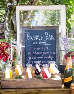 a table topped with bottles and glasses filled with liquid next to a chalkboard sign