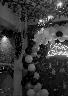 black and white photo of happy birthday sign with balloons hanging from the ceiling in front of it