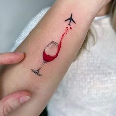 a woman's arm with a red wine glass and an airplane tattoo on it