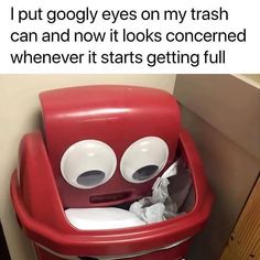 a red trash can with two eyes on it's lid and tissue paper in the bottom