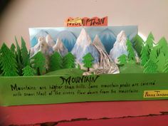 a mountain scene made out of paper with trees and mountains in the background on display