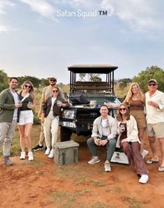 a group of people posing for a photo in front of a safari vehicle on dirt ground