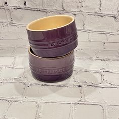 two purple cups sitting on top of each other in front of a white brick wall