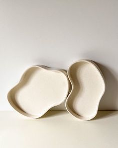 two white plates sitting next to each other on top of a table, one is shaped like an egg