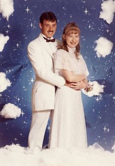 a man and woman dressed in white posing for a photo with clouds on the background