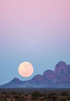 the full moon is setting over the mountains