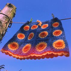 a crocheted blanket hanging on a clothes line with a tree in the background