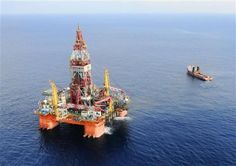 an oil rig in the middle of the ocean next to a boat on the water