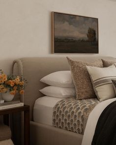 a bed with white sheets, pillows and a painting hanging on the wall above it