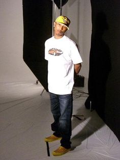 a man standing in front of a black backdrop wearing yellow shoes and a white t - shirt