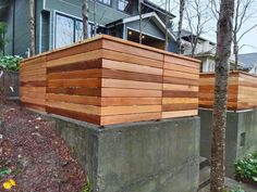 a large wooden box sitting on top of a cement wall next to some trees and bushes