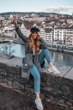 a woman sitting on top of a stone wall with her arms up in the air