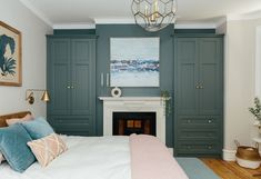 a bedroom with green painted cabinets and a white bed in front of a fire place