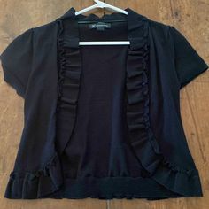 a black top with ruffles hanging on a hanger next to a wooden floor