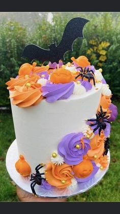 a white cake with purple and orange flowers on it, topped with a black bat