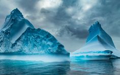 two icebergs floating in the ocean under a cloudy sky