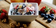 a bowl filled with fruit and nuts on top of a wooden table next to apples