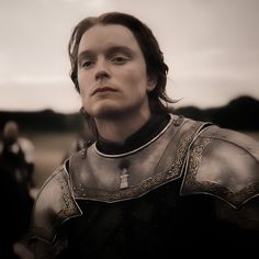 a man with long hair wearing armor and looking off into the distance in front of other people