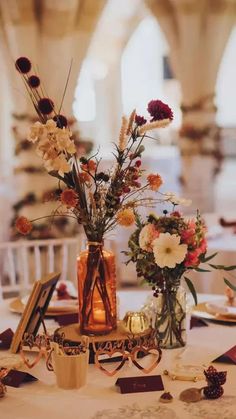 two vases filled with flowers sitting on top of a white tablecloth covered table